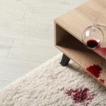 Umgestürztes Glas und verschütteter Rotwein auf weißem Teppich