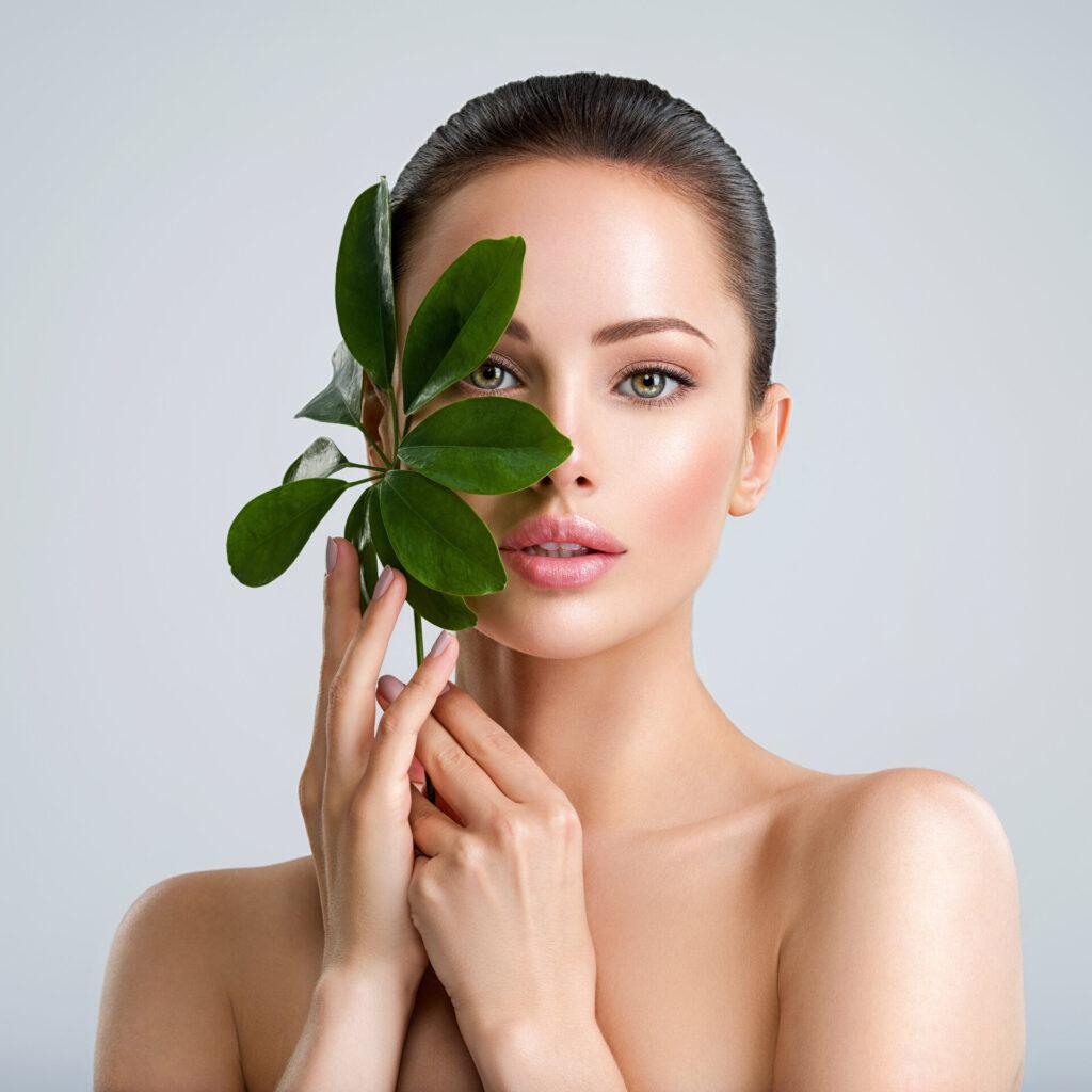 Schöne Frau mit grünen Blättern in der Nähe von Gesicht und Körper. Konzept der Schönheitsbehandlungen für die Hautpflege