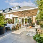 Strukturierter Garten mit Gabionensteinen, Terrasse, Sonnenschirm und hoher Bepflanzung als Sichtschutz