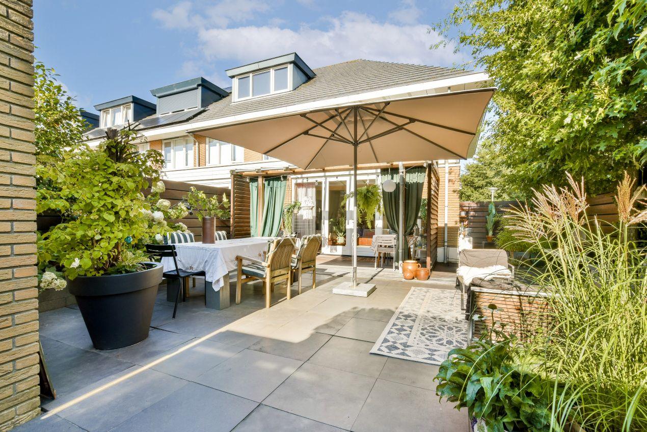 Strukturierter Garten mit Gabionensteinen, Terrasse, Sonnenschirm und hoher Bepflanzung als Sichtschutz